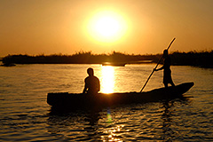 pirogue or fishing boat with two people aboard, in front of sunset on Lake Chad