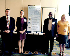 Symposium attendees standing in front of table and poster