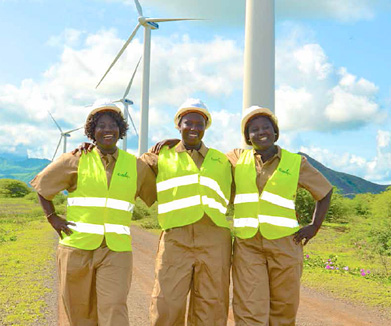three women wearing safety vests and helmets standing in front of wind turbines